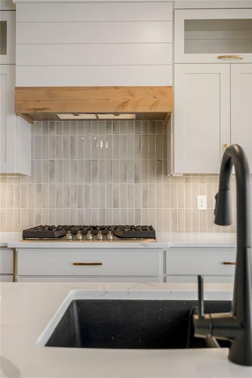 details with stainless steel gas stovetop, light countertops, backsplash, and white cabinets