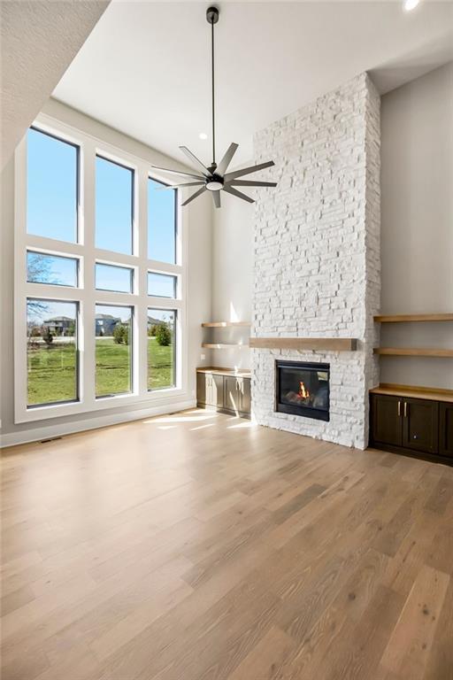 unfurnished living room with ceiling fan, a towering ceiling, a fireplace, and wood finished floors