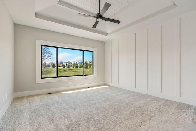 carpeted empty room featuring a ceiling fan, a raised ceiling, and visible vents