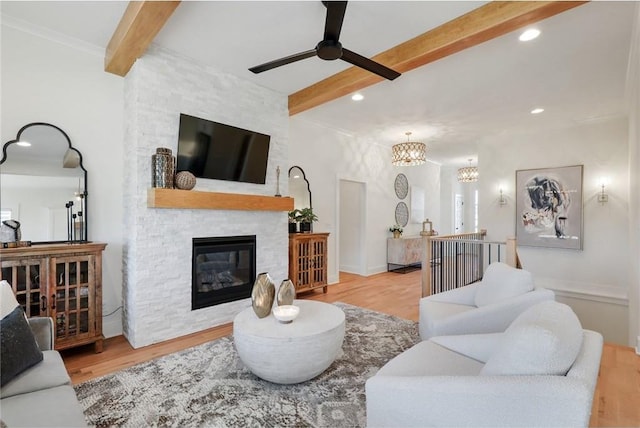 living room featuring beam ceiling, ceiling fan with notable chandelier, a fireplace, and light wood-type flooring