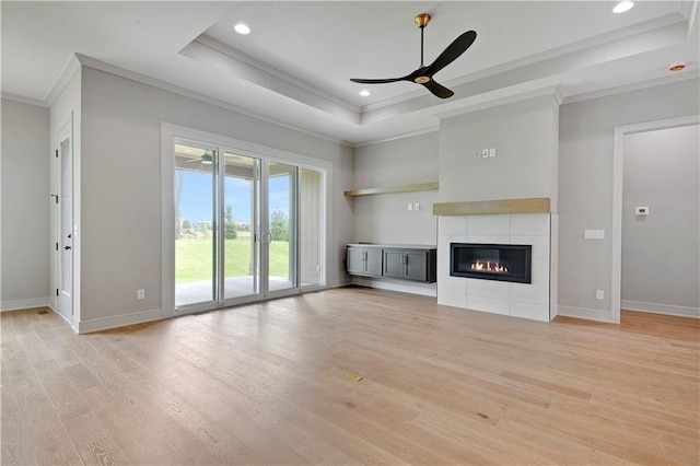 24940 W 98th Pl, Lenexa, KS 66227 - unfurnished living room featuring ornamental molding, a raised ceiling, light wood-style floors, ceiling fan, and a tiled fireplace