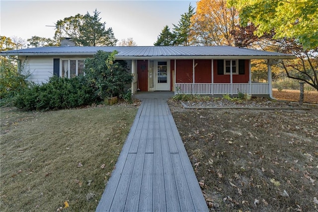 single story home featuring metal roof, a porch, a chimney, and a front lawn