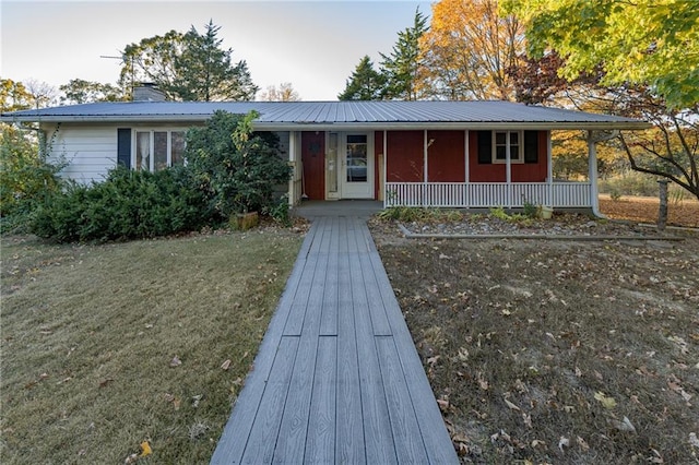 single story home with covered porch, a chimney, metal roof, and a front lawn