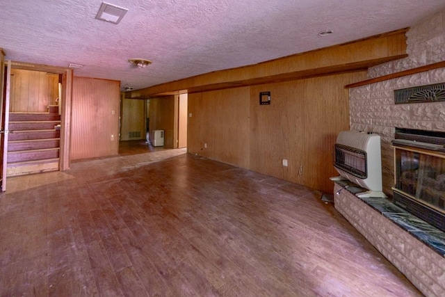 unfurnished living room featuring a stone fireplace, hardwood / wood-style flooring, wooden walls, heating unit, and a textured ceiling