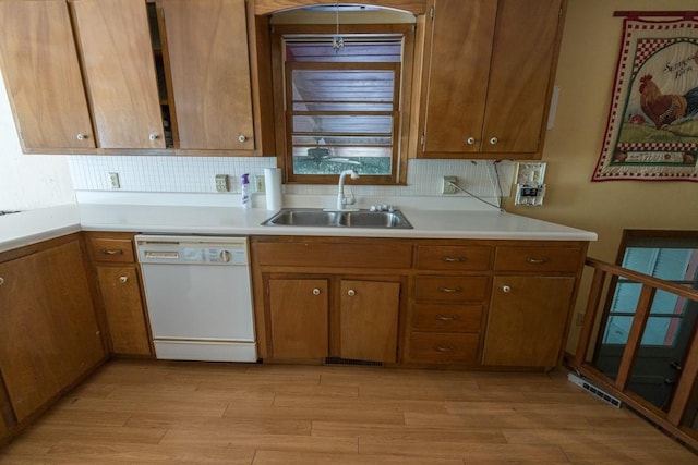 kitchen with backsplash, white dishwasher, sink, and light wood-type flooring