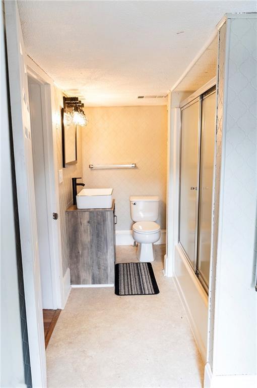 full bathroom featuring bath / shower combo with glass door, vanity, toilet, and concrete flooring