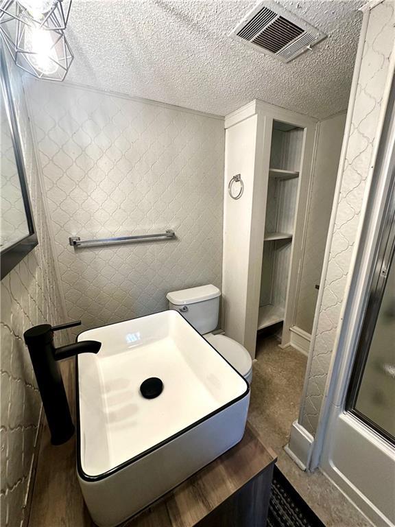 bathroom featuring enclosed tub / shower combo, a textured ceiling, and toilet