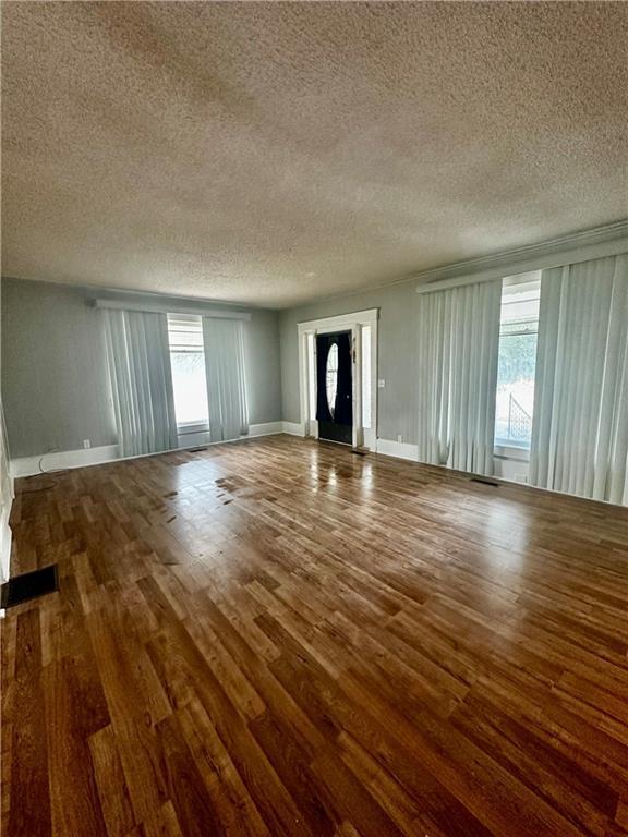 unfurnished living room featuring a textured ceiling, dark wood-type flooring, and a wealth of natural light