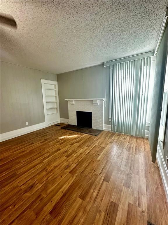 unfurnished living room with a textured ceiling, wood-type flooring, and a brick fireplace