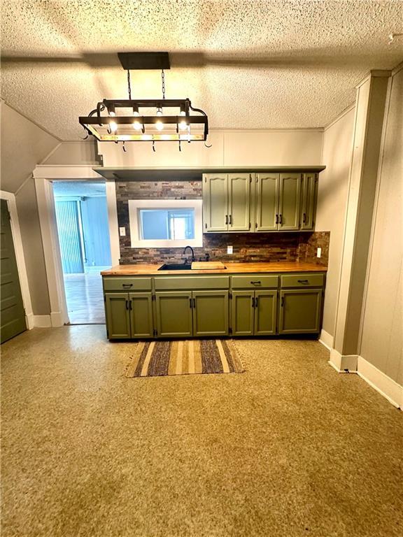 kitchen with decorative backsplash, green cabinetry, a textured ceiling, sink, and light carpet