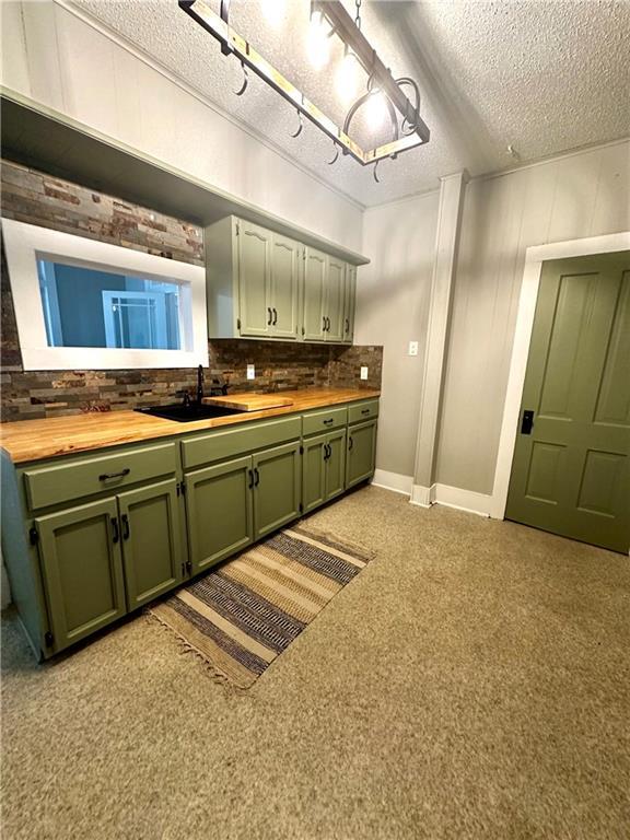 kitchen with decorative backsplash, butcher block counters, a textured ceiling, sink, and green cabinets