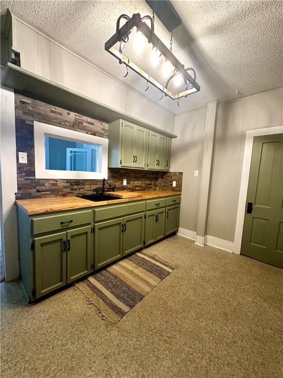 kitchen with a textured ceiling, sink, green cabinets, backsplash, and butcher block countertops