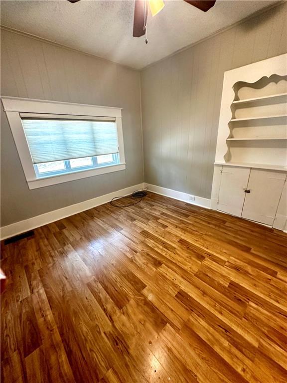 spare room with wooden walls, ceiling fan, hardwood / wood-style floors, and a textured ceiling