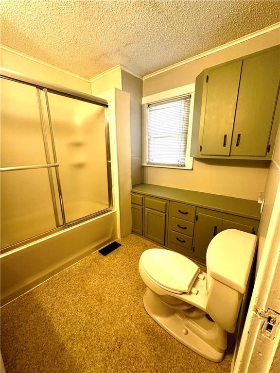 bathroom with a textured ceiling, crown molding, enclosed tub / shower combo, and toilet