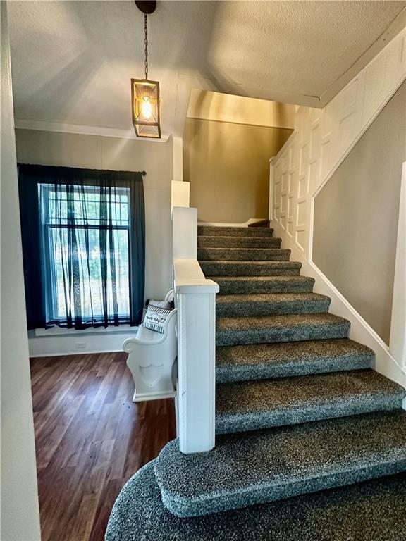 stairway with a textured ceiling, hardwood / wood-style flooring, and crown molding