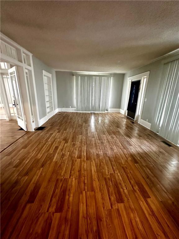 unfurnished room featuring a textured ceiling, built in shelves, and hardwood / wood-style floors