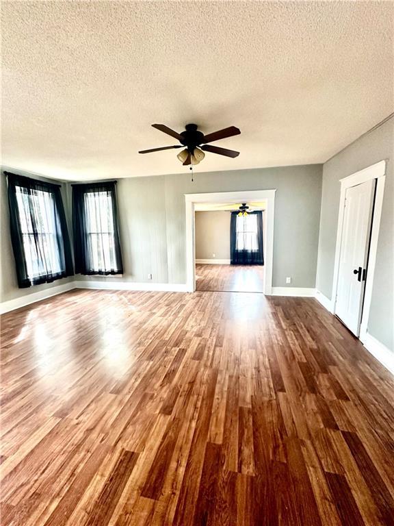 unfurnished living room featuring ceiling fan, hardwood / wood-style flooring, and a textured ceiling