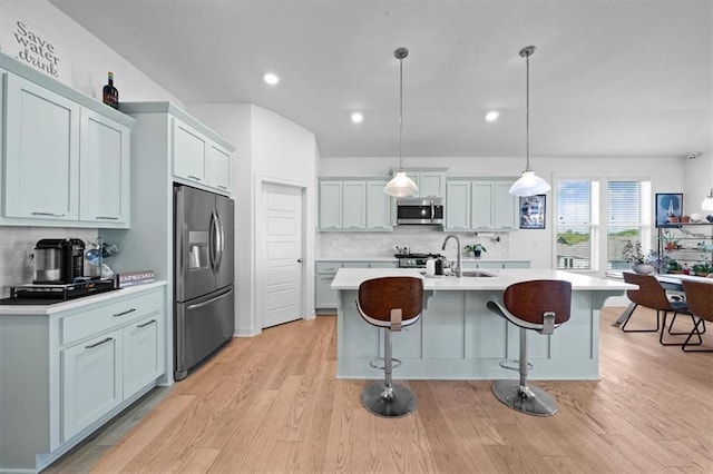 kitchen with appliances with stainless steel finishes, a breakfast bar, an island with sink, sink, and hanging light fixtures