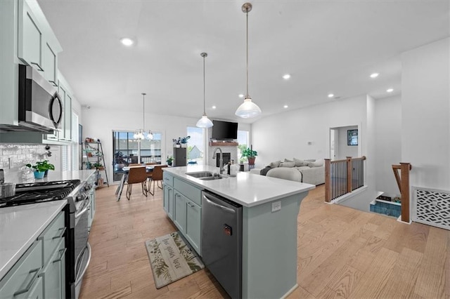 kitchen featuring sink, hanging light fixtures, light wood-type flooring, stainless steel appliances, and a kitchen island with sink