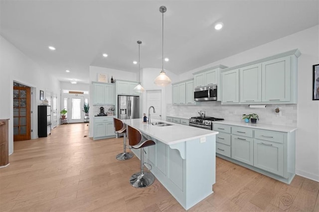 kitchen with a breakfast bar, sink, appliances with stainless steel finishes, an island with sink, and pendant lighting