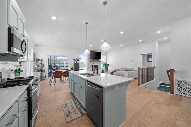 kitchen with sink, light wood-type flooring, appliances with stainless steel finishes, pendant lighting, and a kitchen island with sink