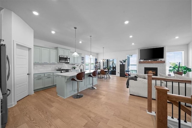 kitchen featuring a breakfast bar, decorative light fixtures, light wood-type flooring, stainless steel appliances, and a kitchen island with sink