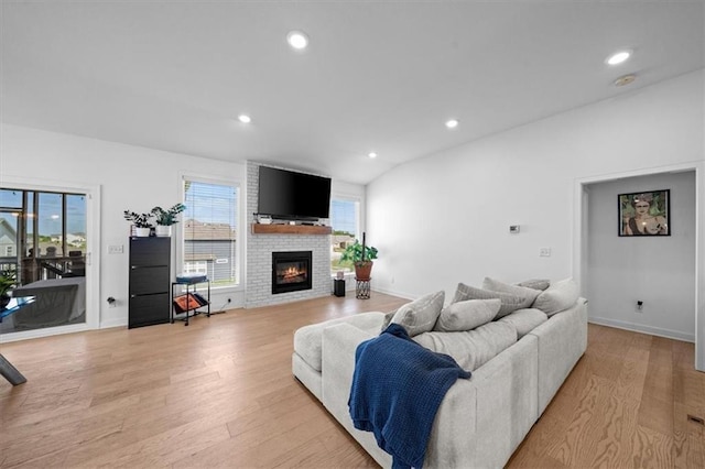 living room featuring vaulted ceiling, light hardwood / wood-style floors, and a brick fireplace