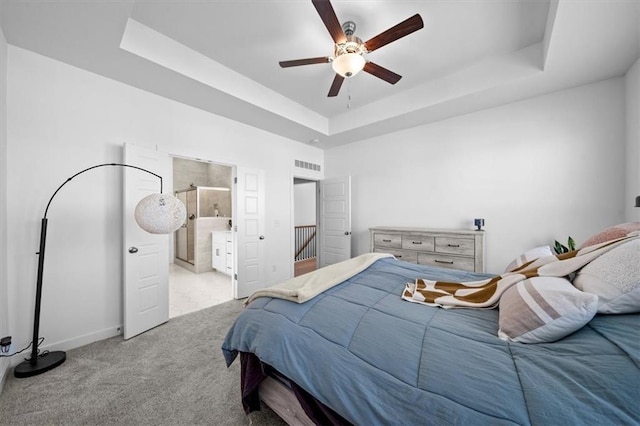 bedroom featuring ceiling fan, light colored carpet, a raised ceiling, and ensuite bath