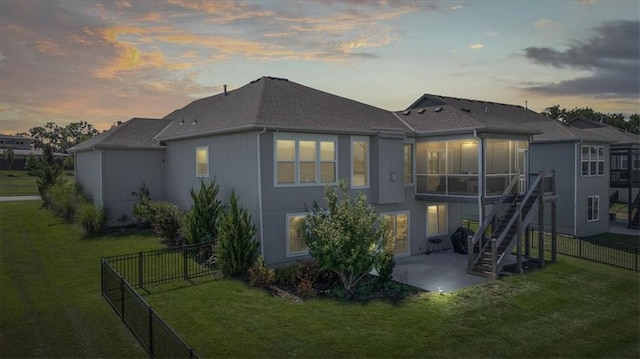 back house at dusk with a patio, a sunroom, and a lawn