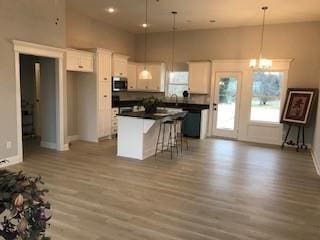 kitchen featuring white cabinetry, a chandelier, light wood-type flooring, a kitchen island, and a towering ceiling