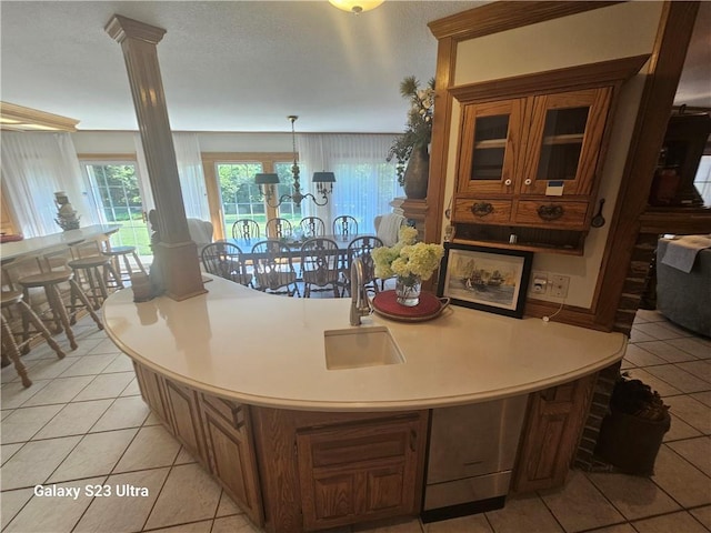 kitchen with a center island with sink, light tile patterned floors, hanging light fixtures, and ornate columns