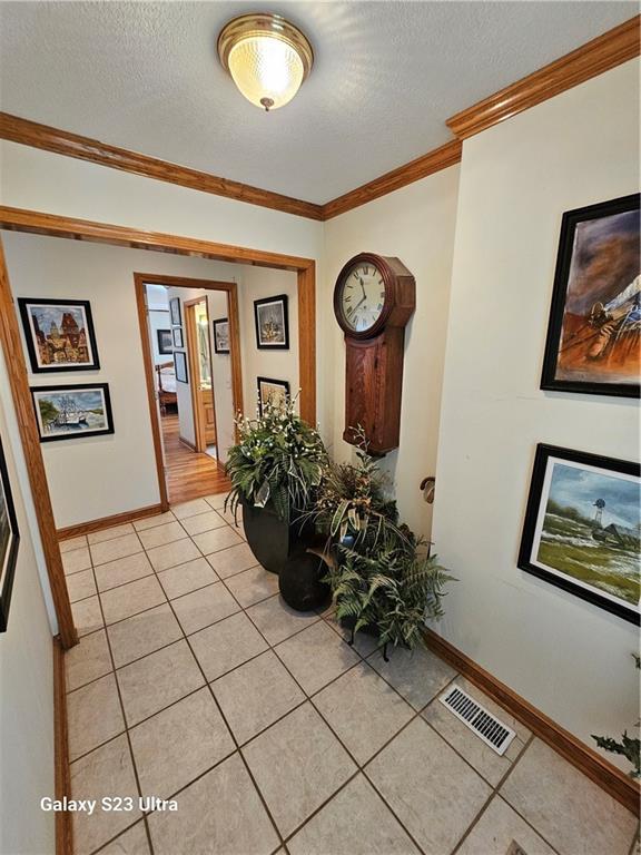 corridor featuring crown molding, a textured ceiling, and light tile patterned floors