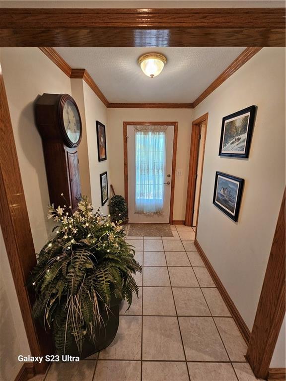 doorway featuring crown molding, light tile patterned floors, and a textured ceiling