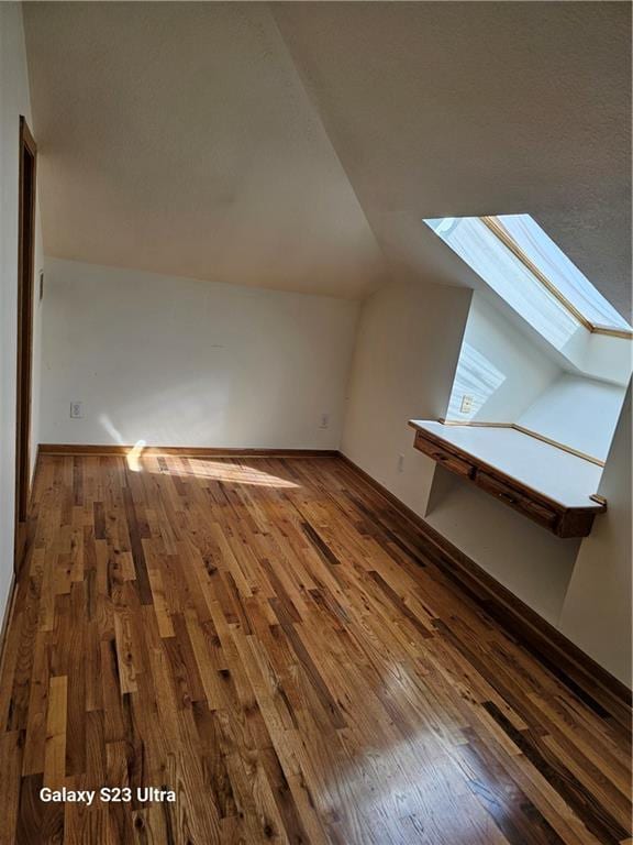 bonus room featuring dark wood-type flooring and vaulted ceiling with skylight