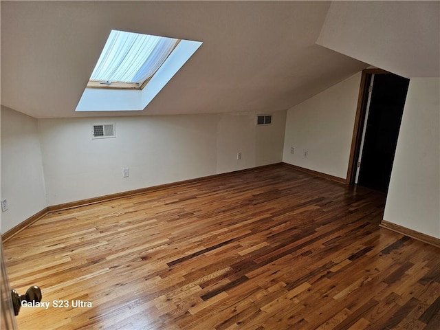 additional living space with hardwood / wood-style flooring and vaulted ceiling with skylight