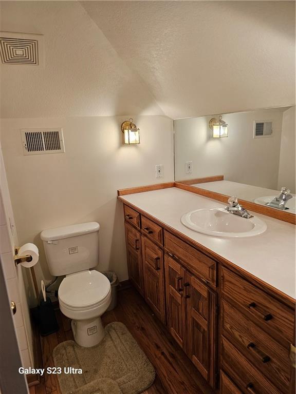 bathroom featuring vaulted ceiling, wood-type flooring, vanity, toilet, and a textured ceiling