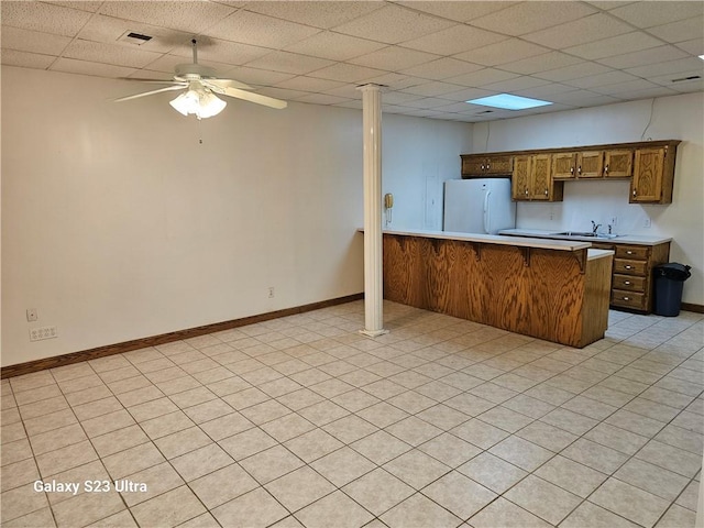 kitchen featuring sink, white refrigerator, ceiling fan, kitchen peninsula, and a drop ceiling