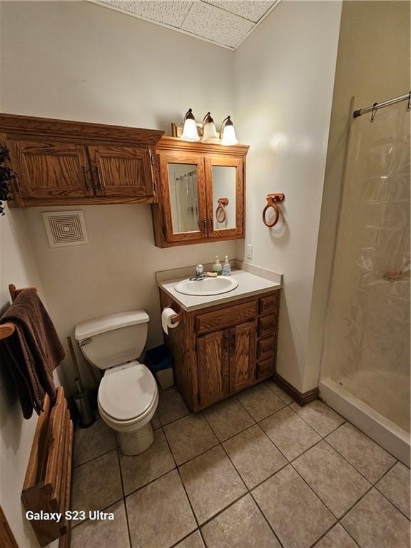 bathroom with a paneled ceiling, tile patterned flooring, vanity, toilet, and walk in shower