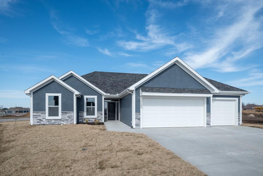 view of front of property featuring stucco siding, a front yard, a garage, stone siding, and driveway