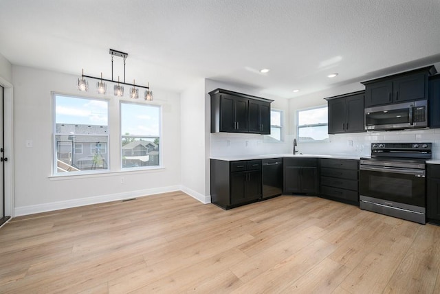 kitchen featuring backsplash, appliances with stainless steel finishes, decorative light fixtures, and light wood-type flooring