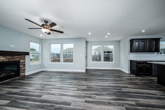 unfurnished living room featuring a stone fireplace, a ceiling fan, dark wood-style flooring, and baseboards