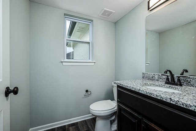 half bath featuring visible vents, toilet, wood finished floors, baseboards, and vanity