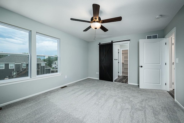 unfurnished bedroom with a barn door, baseboards, visible vents, and carpet floors