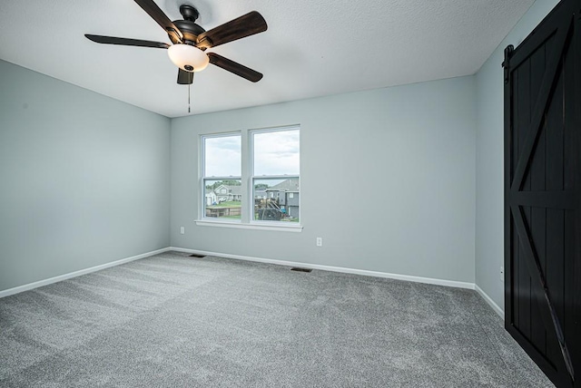 carpeted empty room featuring baseboards, visible vents, ceiling fan, a textured ceiling, and a barn door