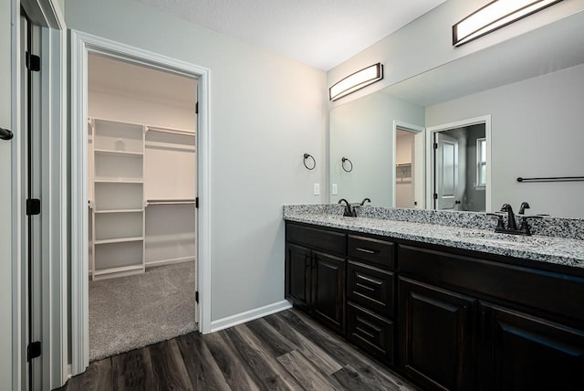 bathroom featuring a spacious closet, baseboards, double vanity, wood finished floors, and a sink