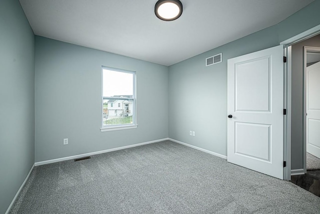 spare room featuring dark colored carpet, visible vents, and baseboards