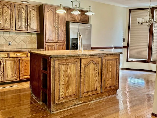 kitchen with an inviting chandelier, light hardwood / wood-style flooring, stainless steel fridge, decorative light fixtures, and a center island with sink