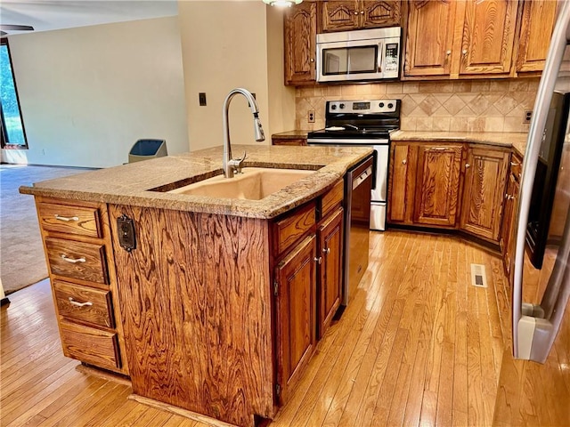 kitchen featuring sink, an island with sink, stainless steel appliances, and light hardwood / wood-style floors