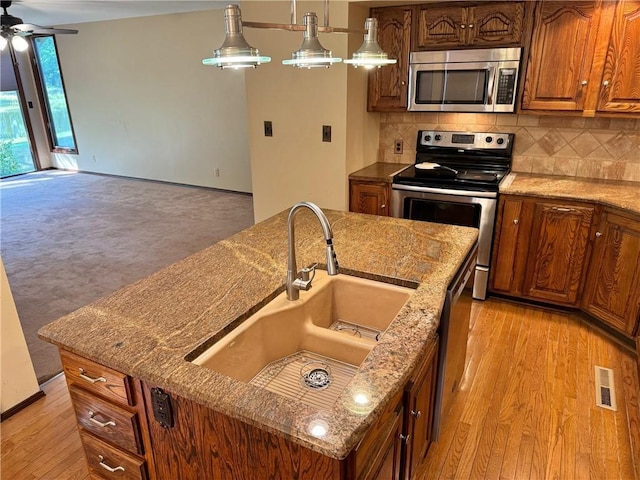 kitchen featuring light stone countertops, light hardwood / wood-style flooring, backsplash, decorative light fixtures, and appliances with stainless steel finishes