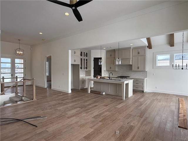 kitchen featuring tasteful backsplash, ceiling fan with notable chandelier, beam ceiling, hanging light fixtures, and an island with sink